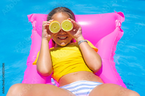 Girl wearing bikini having fun in the pool with lemons as sunglasses on a pink mat.