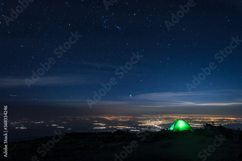 Acampando en la cima de la montaña observando la ciudad de Puebla con un cielo estrellado con la constelación de orión 