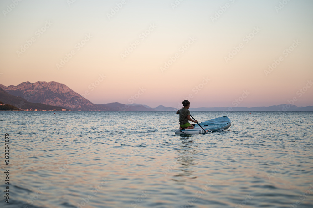 Naklejka premium Boy sitting on the rear end of sup board