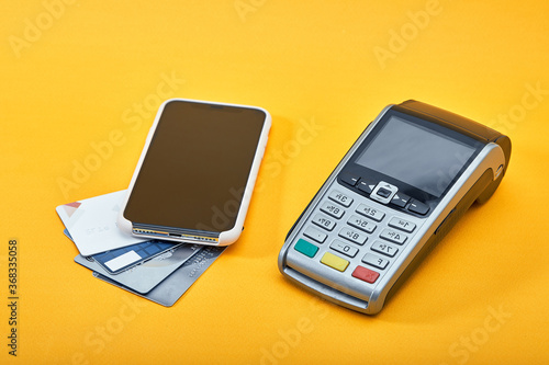 Wireless payment terminal for credit card or NFC payments, cell phone and credit card on yellow background. Copy space for advertising, panorama