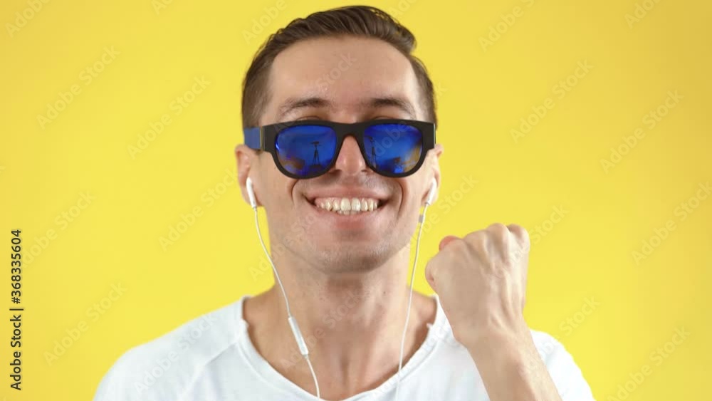 Excited man celebrating success in studio. Portrait of happy person shoots sunglasses and showing yes gesture. Joyful male holding hands up on yellow background. Happy man smiling in slow motion Excited man celebrating success in studio. Portrait of happy person shoots sunglasses and showing yes gesture. Joyful male holding hands up on yellow background. Happy man smiling in slow motion