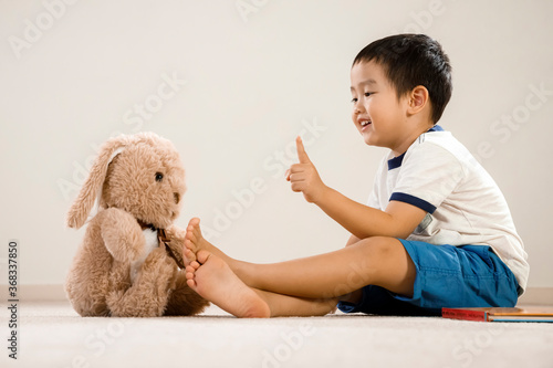 Asian boy with teddy bear, Vietnamese toddler pointing and talking to stuffed toy, cute kid sitting on floor communicating with his favorite toy friend