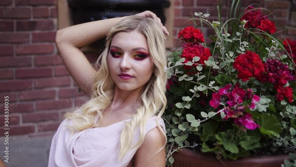 Beautiful blonde in a pink long dress sits in a castle near red flowers Beautiful blonde in a pink long dress sits in a castle near red flowers