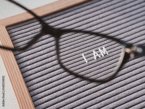 Top view on letterboard with words I AM through eyeglasses. Flat lay concept of psychological self-regulation or gender gender identity. Social psycological issue. Closer look on problems. photo