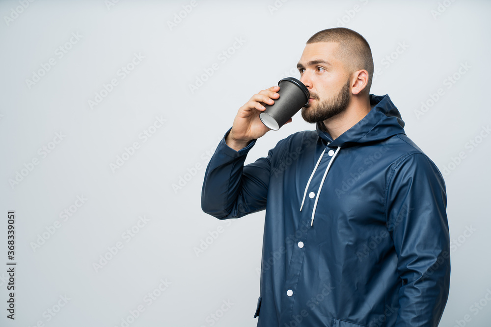 Naklejka premium a man drinks coffee dressed in a blue raincoa