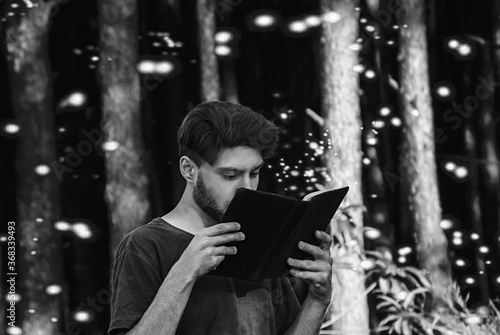 young man reading a book in florest - black white