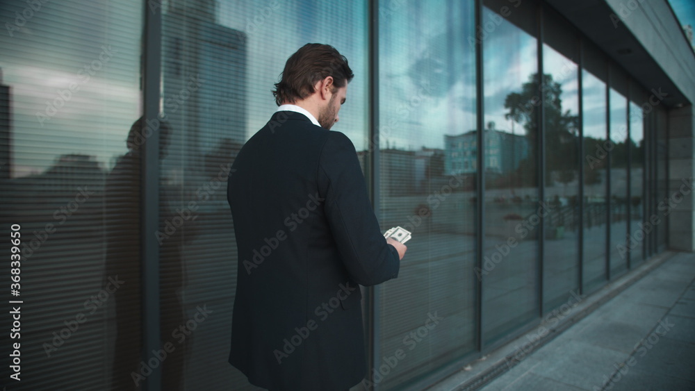 Fototapeta premium Businessman with money walking on street. Male professional counting money