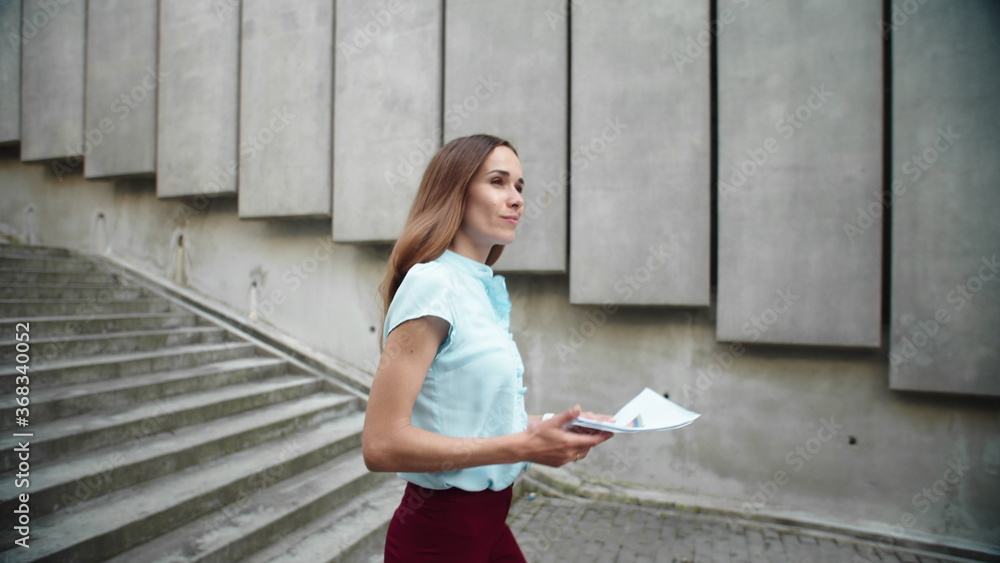 Businesswoman walking downstairs in city. Woman working with business papers Businesswoman walking downstairs in city. Woman working with business papers