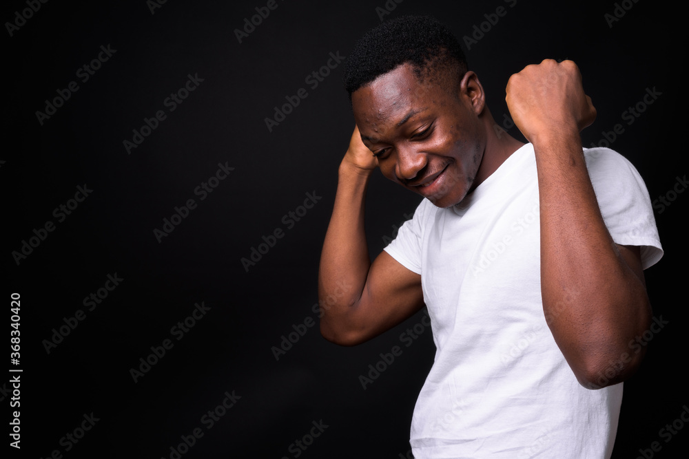 Happy young handsome African man against black background