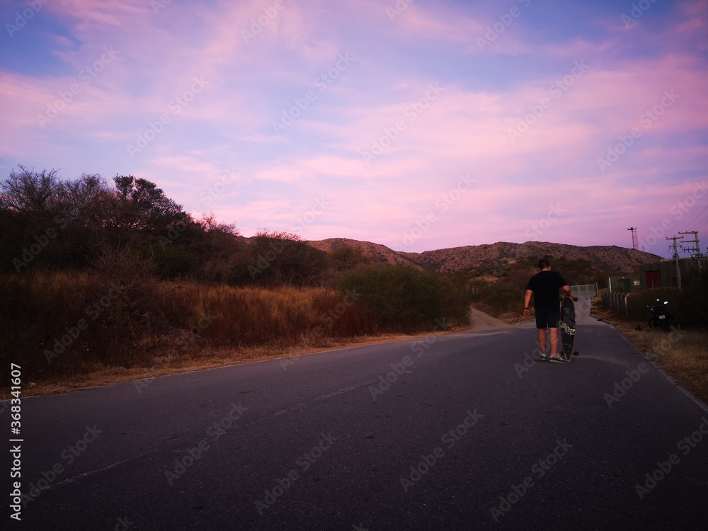 sunset on the road with boy walking on longboard sunset on the road with boy walking on longboard