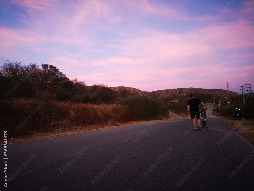 sunset on the road with boy walking on longboard sunset on the road with boy walking on longboard