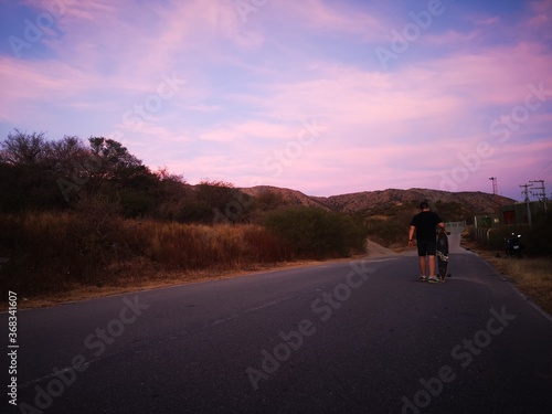 sunset on the road with boy walking on longboard