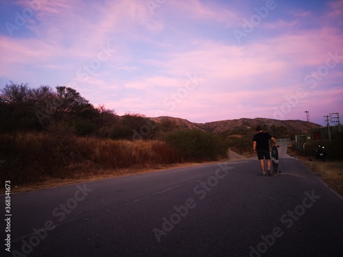 sunset on the road with boy walking on longboard © Uriel