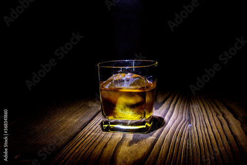 A glass of whiskey on a dark wood table on a dark background.