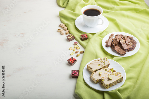 traditional arabic sweets sesame halva with chocolate and pistachio and a cup of coffee on white wooden background. side view, copy space.