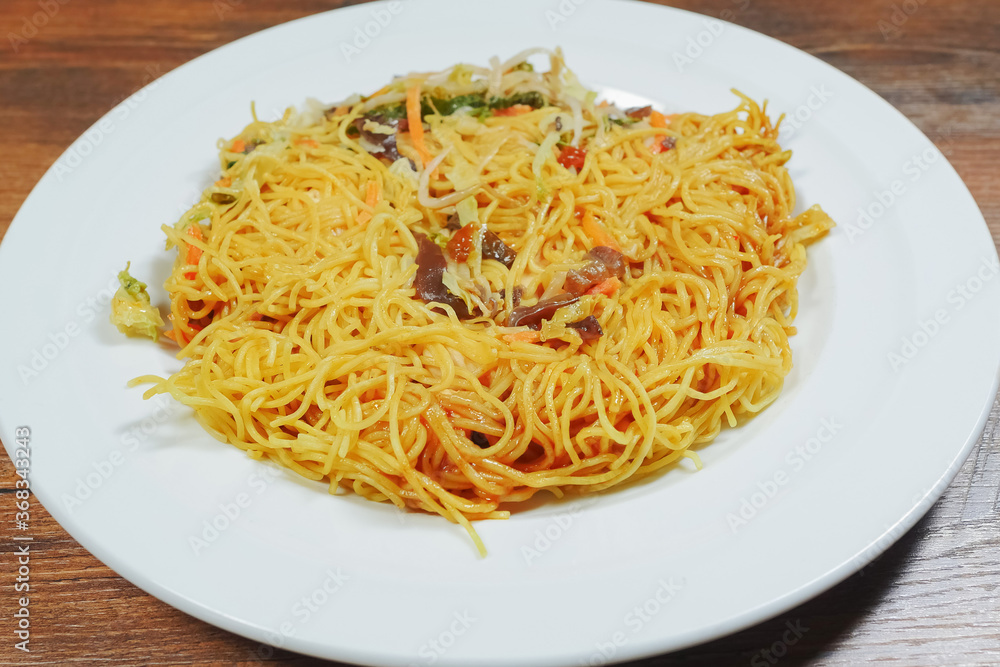 Simple chicken chow mein meal on a white plate and on a wooden table. Chinese style tasty noodles with sauce and vegetables. Concept dinner, Asian flavor.