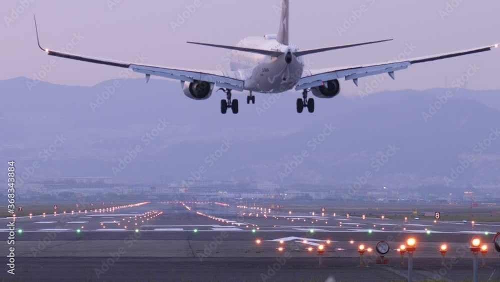 Slow motion shot of landing jet liner, rear view from end of runway. Passenger plane fly down and touch ground. Evening time shot of Itami Airport air traffic