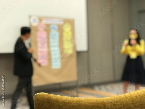 The blurred of the man and woman are standing and speaking in front of the board.