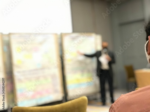 The selective focused on the man is listening the standing man gives a lecture in front of the board.