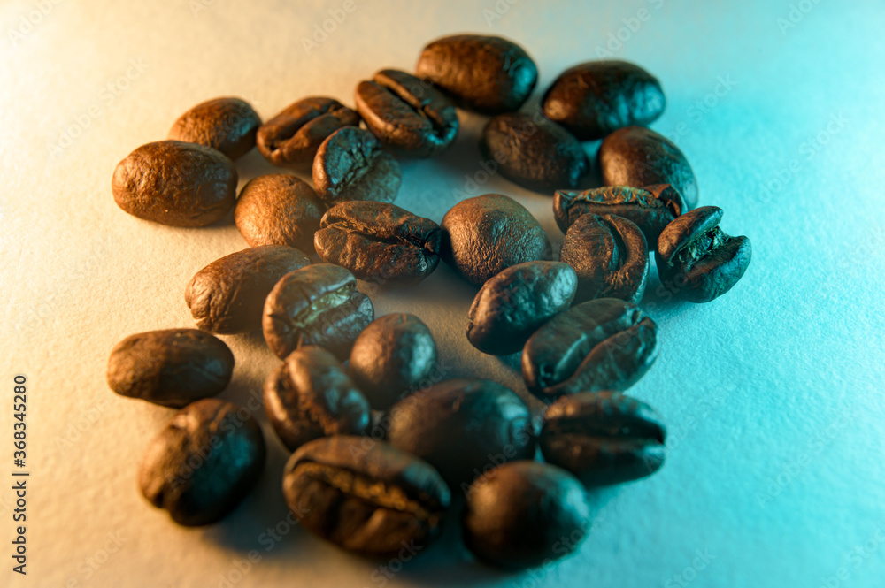 Obraz premium A small heap of roasted coffee beans, isolated on an orange and teal background