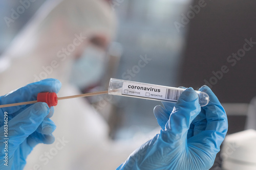 A scientist examining a smear sample in a test tube with a sticker displaying coronavirus positive and negative checkboxes.....