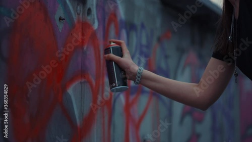 Woman hand painting graffiti on street wall. Girl drawing red heart on building