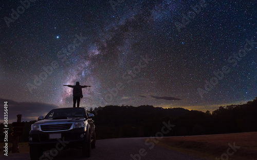 Middle-aged woman Standing refreshing on the roof of the car Looking at the Milky Way in the night sky,Long exposure photograph, with grain.Image contain certain grain or noise and soft focus.