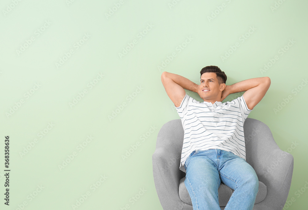 Young man relaxing in armchair near color wall Young man relaxing in armchair near color wall
