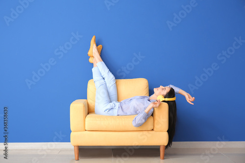 Young woman relaxing in armchair near color wall