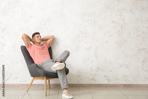 Young man relaxing in armchair near light wall