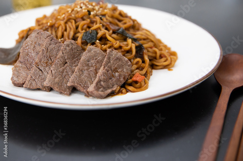 Korean black bean sauce noodles with sliced meat on a plate.