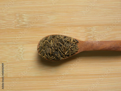 Brown and black color raw whole Bitter cumin seeds on wooden spoon photo