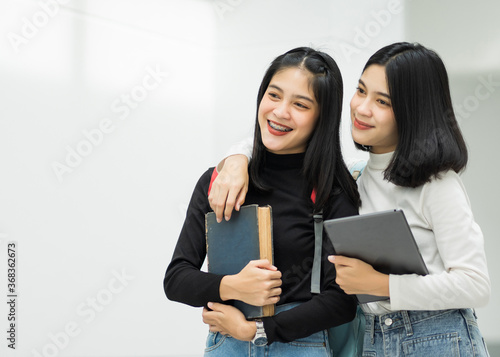 Teenage college friend students walking and chatting in college campus while having break after class. Two happy students walking and talking each other in a campus. Education stock photo.