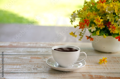 Cups of coffee and vase with beautiful flower bouquet  on table in coffee shop background. © Natwaree