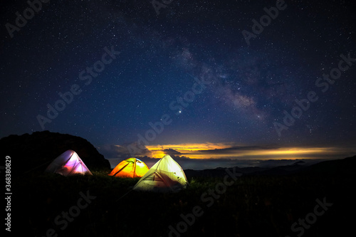 Three tents under the beautiful starry sky glowed in the middle of the night. The orange tent under the Milky way at night.