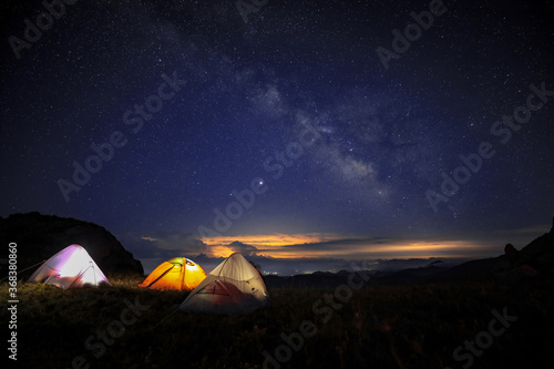 Three tents under the beautiful starry sky glowed in the middle of the night. The orange tent under the Milky way at night.