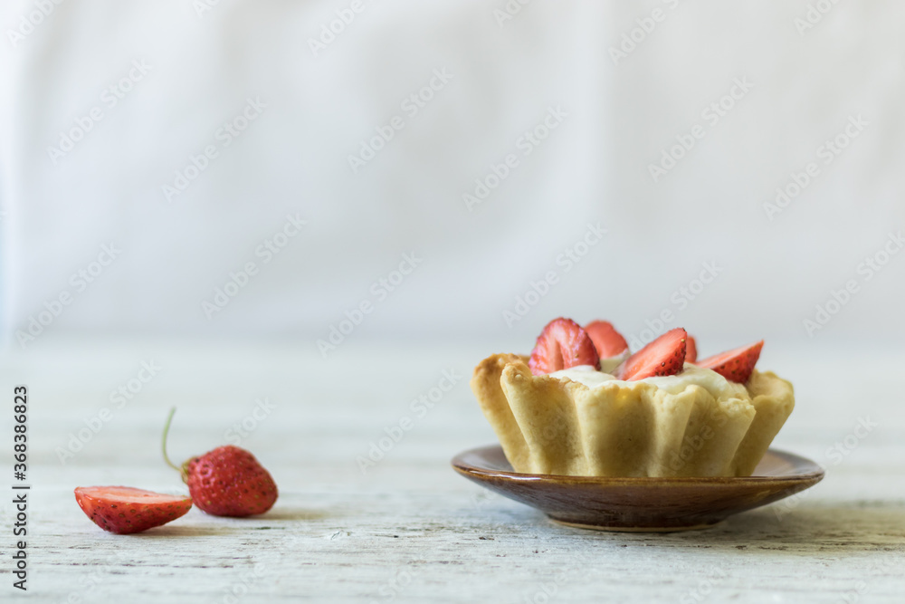 Dessert tartlets with butter cream and fresh strawberries on white wooden background. Horizontal orientation