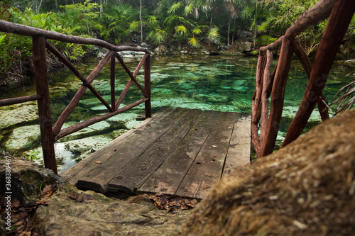 Tropical paradise. Wooden boardwalk leading to an emerald color water cenote in the jungle. Beautiful flora foliage and texture. Transparent natural pond with rocks in the bed.