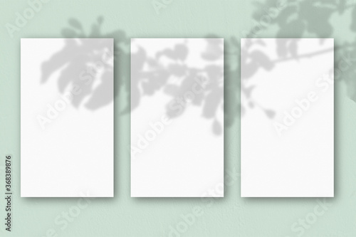 3 vertical sheets of textured white paper on light green table background. Mockup overlay with the plant shadows. Natural light casts shadows from an exotic plant. Horizontal orientation