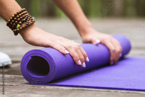 Girl unwinding gymnastic mat for yoga class outdoors, close-up