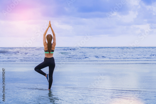 Young woman doing practice yoga on the sea beach at sunset