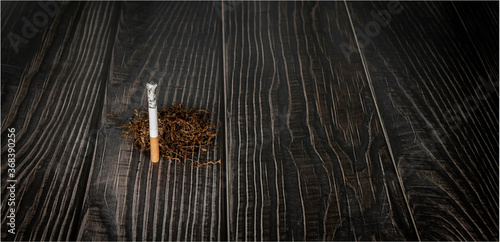 burning cigarette and dried tobacco lay on a wooden background. illness concept.