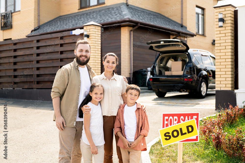 Portrait of smiling young family embracing each other against new house with car, moving concept