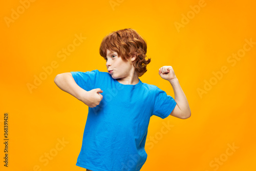 Happy red-haired boy in a blue T-shirt on a yellow background dances