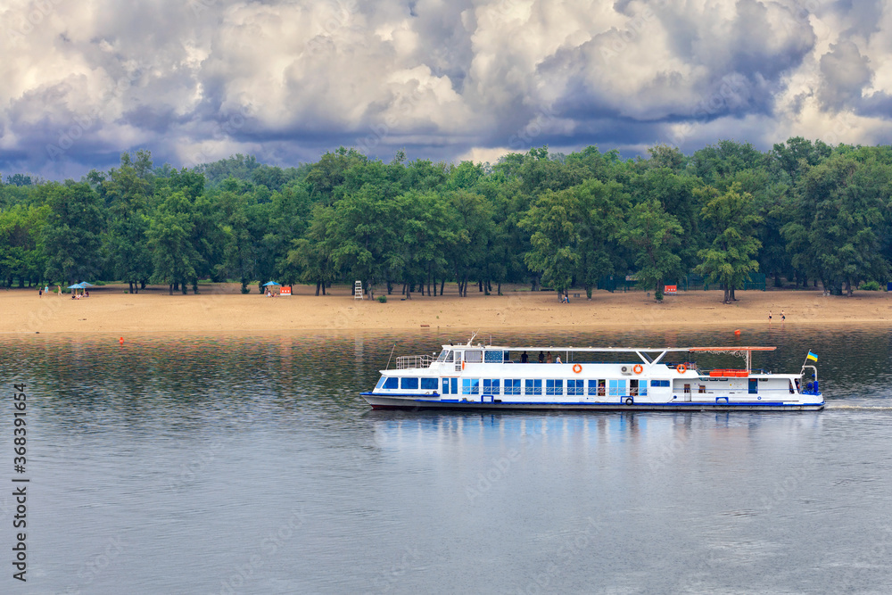 A river tram runs along the banks of the Dnipro against the backdrop of a deserted beach in anticipation of an impending thunderstorm.