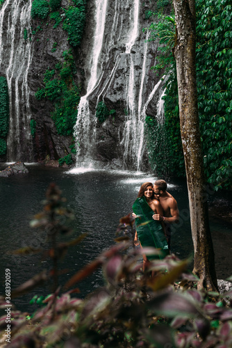 Lovers at the waterfall. Beautiful couple at a waterfall in Indonesia. A couple in love travels around the island of Bali. A man and a woman kiss at the waterfall. Travel to Asia. Сopy space