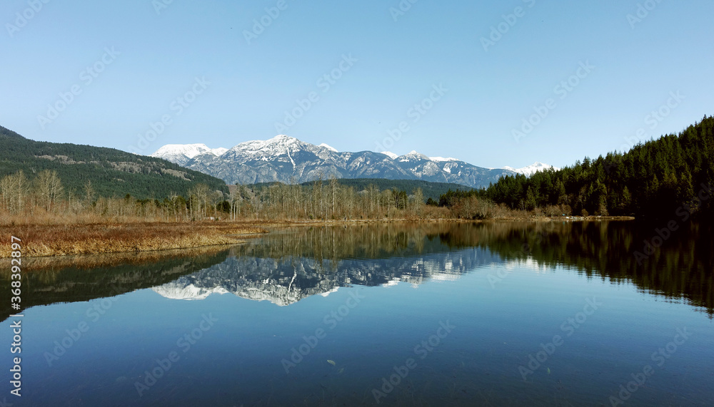 a tranquil scene of One Mile Lake with the reflection of the snow covered mountains in British Columbia Canada, road trip, explore the beauty of local area