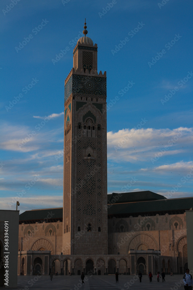 The square with people and the Hassan II Mosque is the largest mosque in Morocco.