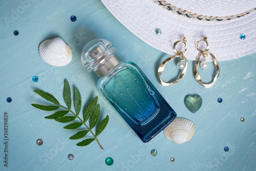 Bottle of perfume, earrings, shells on the blue background