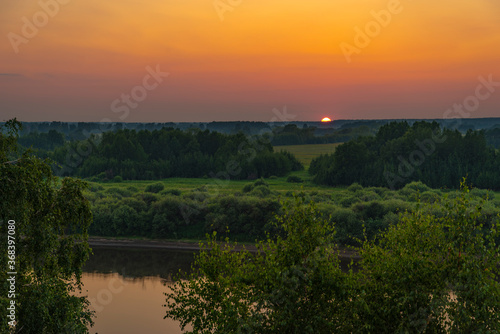 Beautiful views of the sunset over the river with trees  fields and flowers
